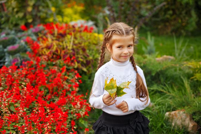Young girl in braids holding autumn leaves among red flowers