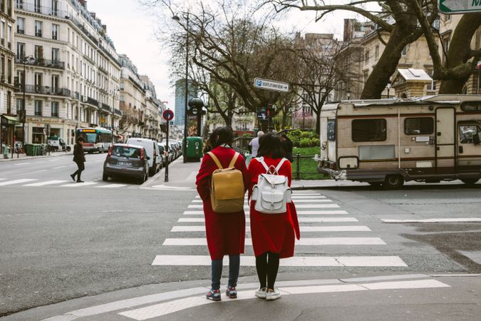 Back view of two girls in red coats and backpacks on pedestrian lane