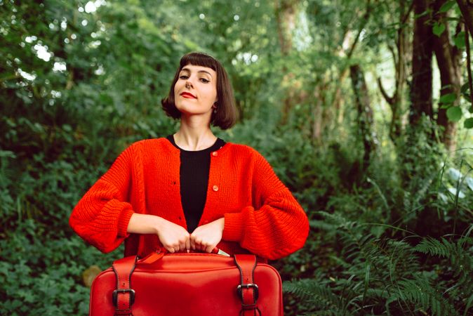 Woman in red with big red suitcase in forest