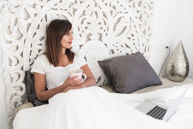 Woman sitting in bed with laptop and cup of coffee
