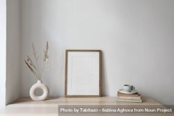 Elegant neutral poster mockup of wooden picture frame on beige table with modern boho vase with dry grass and old books 4ZGzyb