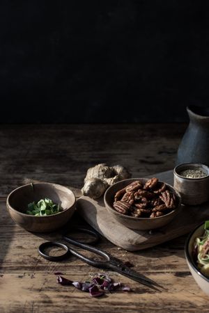 Bowl with pecan nuts near scissors, cutting board, pitcher and ginger