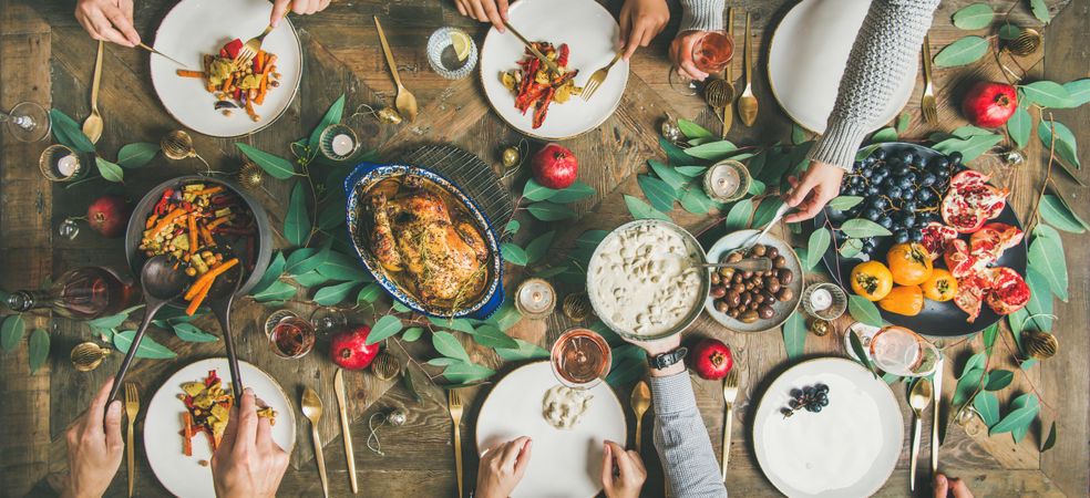 Group serving themselves from festive table with roasted chicken and pomegranates, wide composition