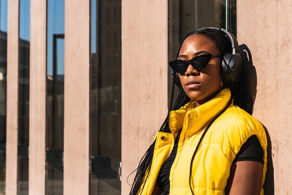 Black woman listening to music while leaning on a wall