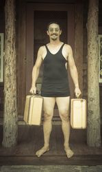 Gentleman Dressed in 1920’s Era Swimsuit Holding Suitcases on Porch