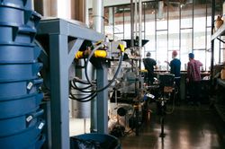 Coffee roaster in foreground with back view of three men at roasting facility