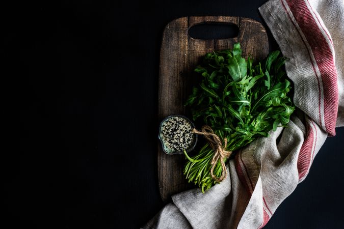 Arugula and sesame seeds on bread board with kitchen towel