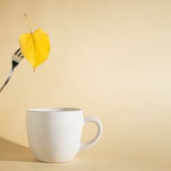 Autumn yellow leaf on a fork above a cup