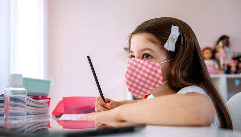 Girl with mask doing homework in her bedroom