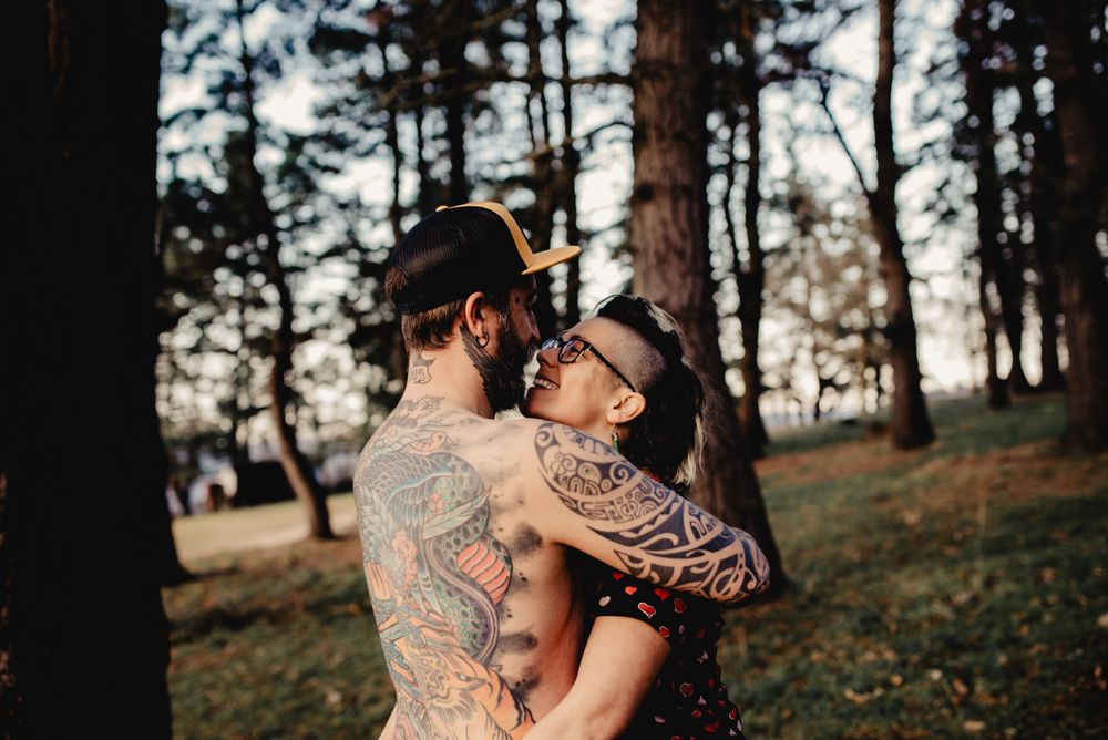 Young guy in tattoos hugging woman in forest