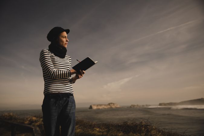 Woman writing in notebook on bench on shore near water