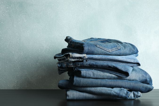 Stack of jeans pants on table, space for text