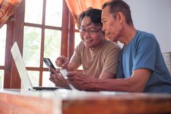 Happy adult son and mature father pay online using laptop and credit card