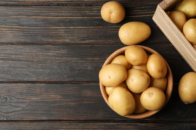 Top view of bowl of potatoes next to basket of potatoes on dark table, copy space