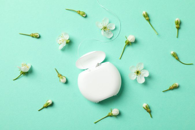 Dental floss and flowers on mint background, top view
