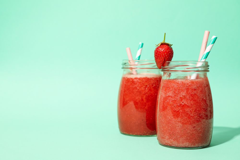 Glass jars with strawberry cocktail on mint background. Summer drink