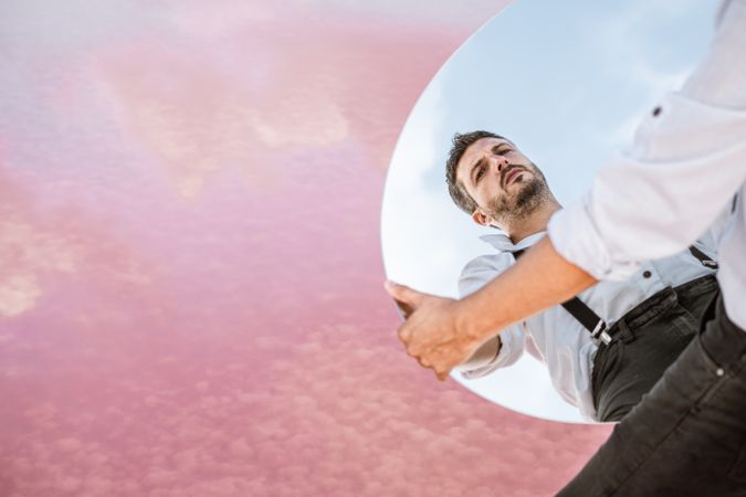 Stylish man holding mirror with reflection