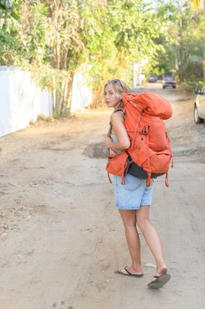Young woman walking along road with backpack