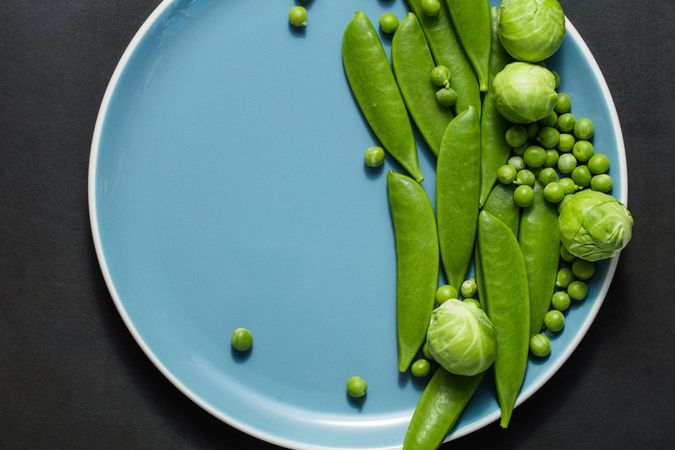 Green peas and brussels sprouts on a blue plate placed on dark background