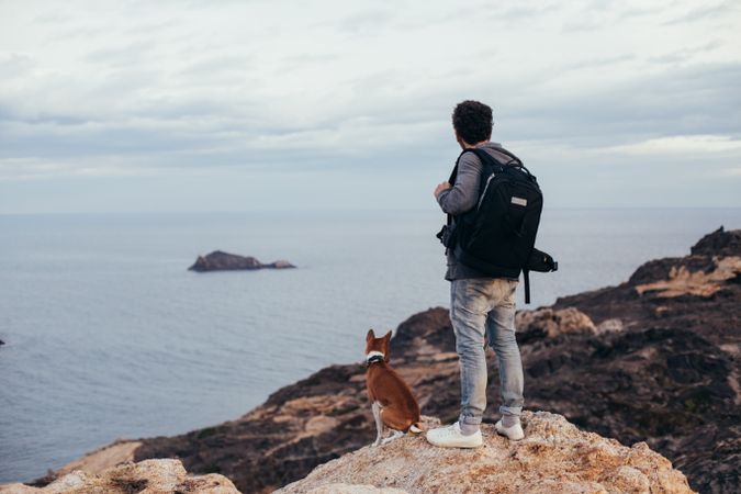Hiker with dog on the coast looking over the sea