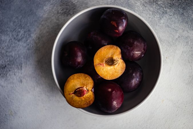 Bowl of halved ripe plums on grey table