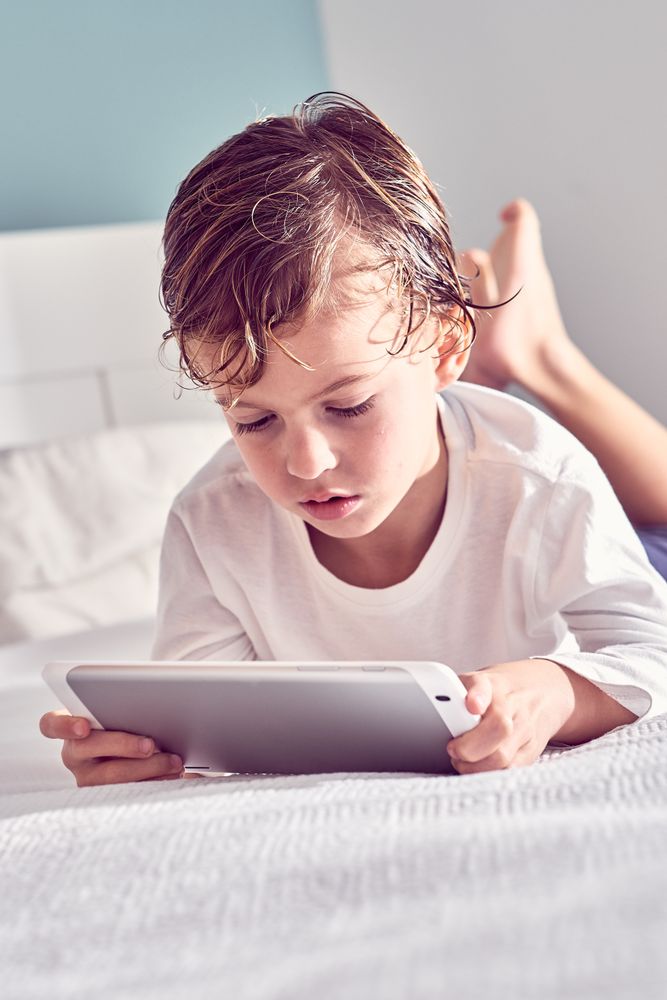 Boy lying on bed and watching video on tablet