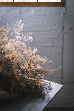Bunch of plant in paper on table near stool in grey room