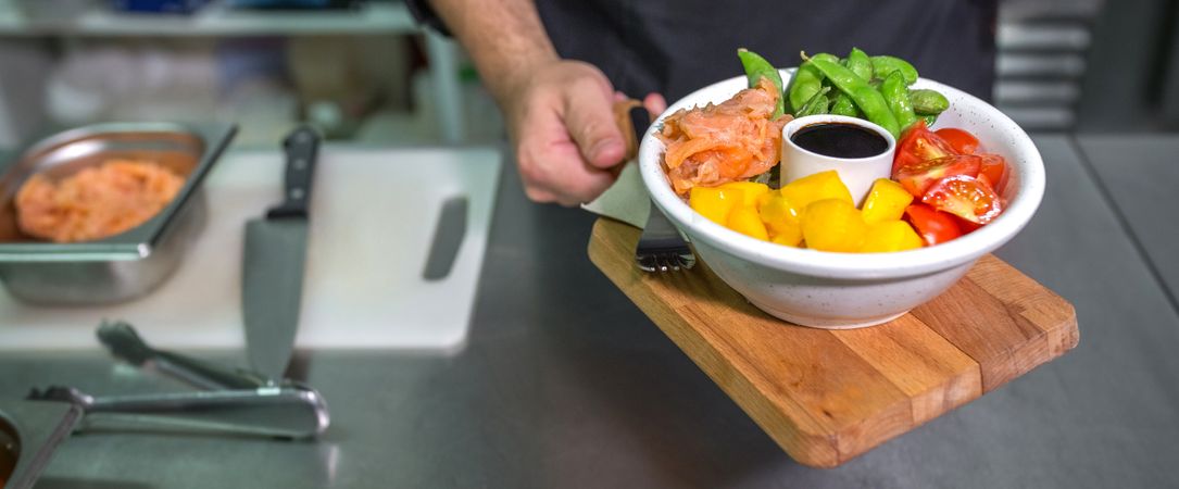 Banner of unrecognizable chef showing fresh colorful poke bowl with salmon on restaurant kitchen