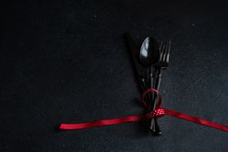 Dark cutlery on dark background tied with festive red ribbon