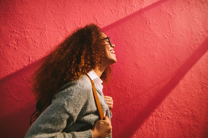 Happy woman with curly hair standing beside red wall