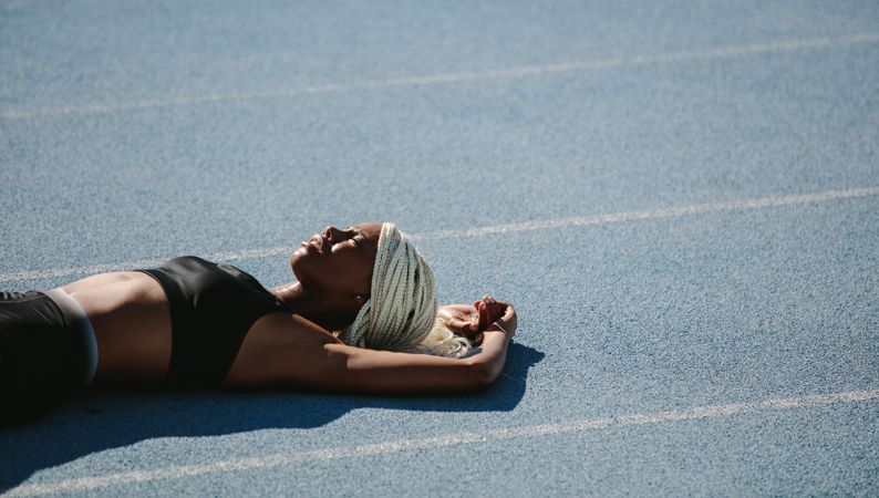 Woman athlete lying on the running track relaxing in the sun after workout