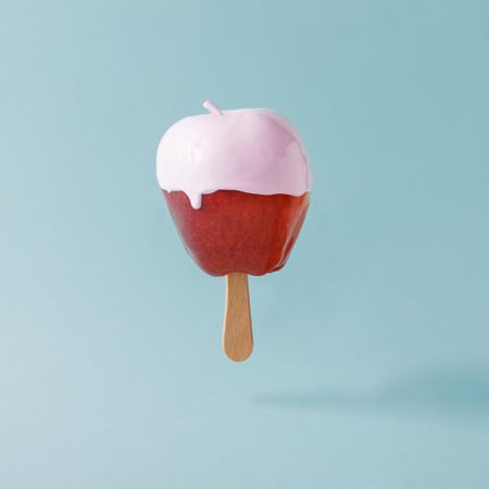 Apple on stick with pink syrup on pastel blue background