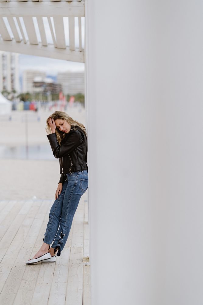 Smiling trendy woman leaning on white pillar on seashore