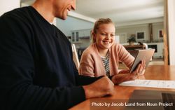Father and daughter sitting at table using a digital tablet together at home 5wrkL0