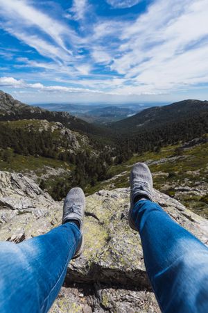 Person sitting dangling legs on stone above mountain valley
