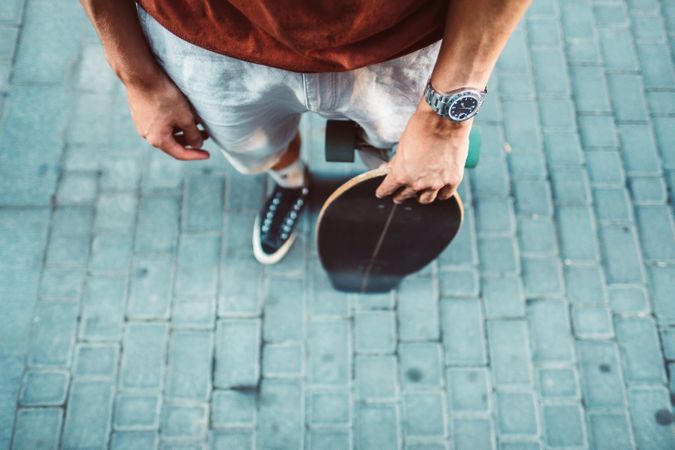 Sportive man carrying longboard while standing on street