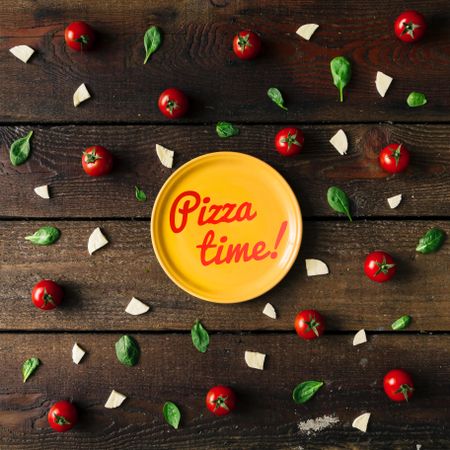 Basil, tomatoes, and cheese on wooden background with plate and “Pizza time!” text