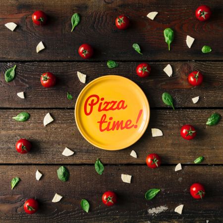 Basil, tomatoes, and cheese on wooden background with plate and “Pizza time!” text