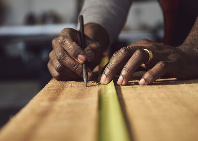 Black man marking measurements along a piece of wood
