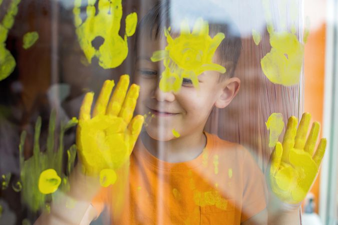 Boy printing window glass with yellow paint