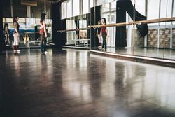 Two young ballerinas in front of big wall mirror training together in studio.