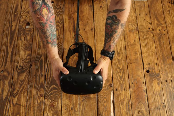 Tattooed hands hold virtual reality goggles