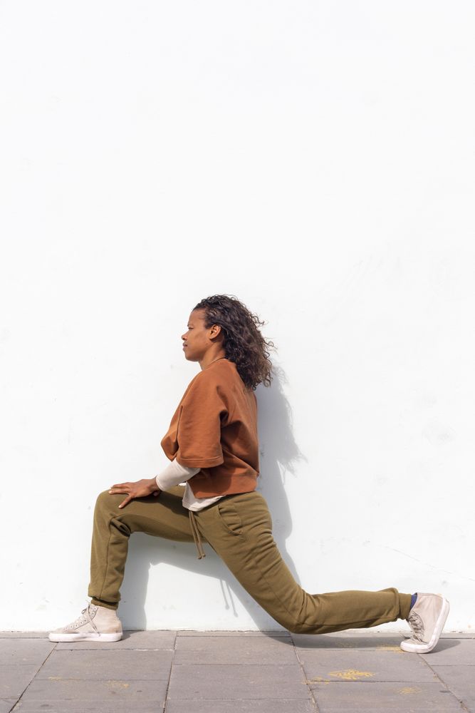 Stylish young female runner in sportswear stretching before running against wall