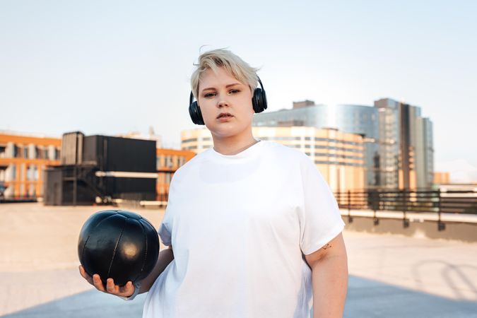 Serious blond woman with medicine ball and headphones on a rooftop