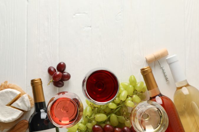 Grape, cheese, bottles and glasses with different wine on light wooden background, copy space