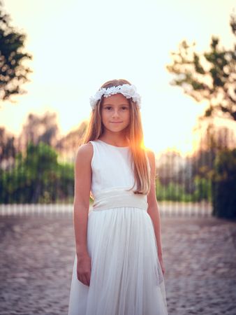 Smiling girl in white dress standing against sunset sky