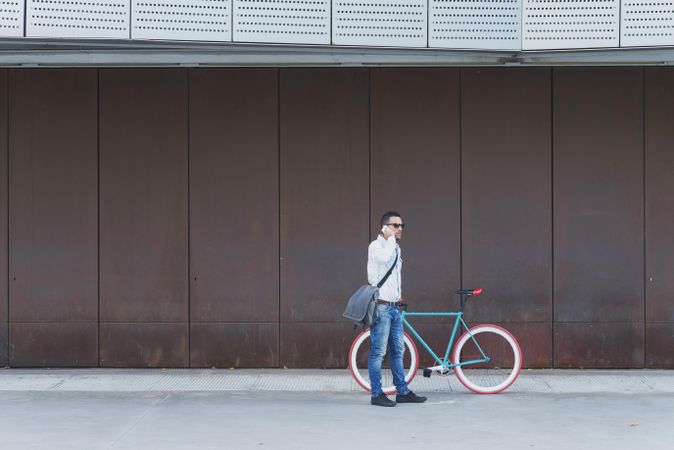 Male in sunglasses standing with red and green bicycle taking call on cell phone