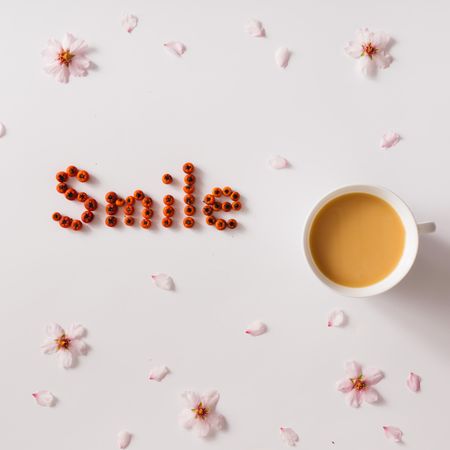 "Smile" text made of red berries with cup of coffee or tea and flowers