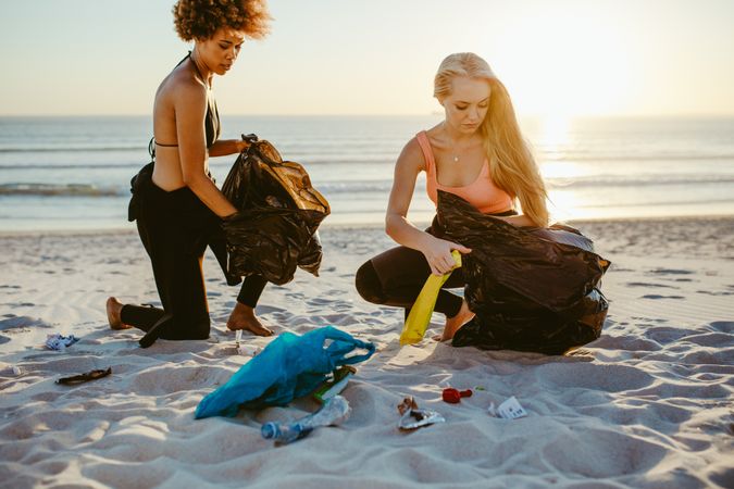 Two female surfers picking up litter on the beach