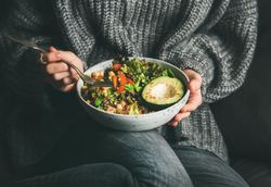 Woman in jeans and sweater eating fresh salad